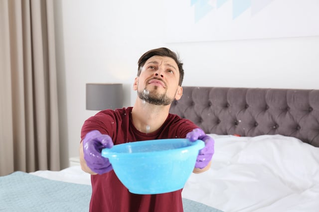 roof repair needed as gentleman holds bucket collecting water from roof leak roof repair needed as gentleman holds bucket collecting water from roof leak